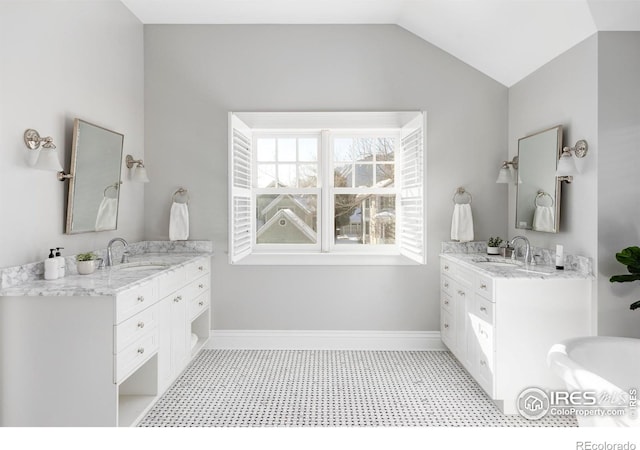 full bathroom featuring two vanities, lofted ceiling, a sink, and baseboards