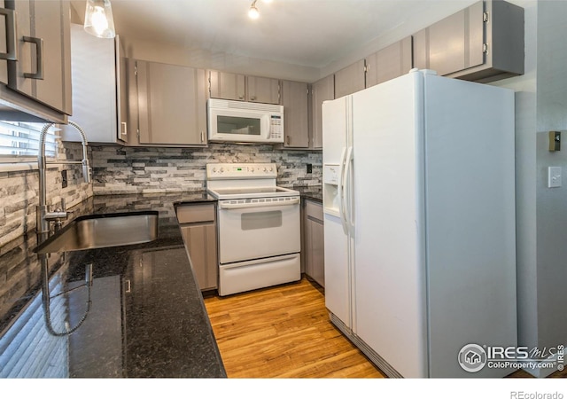 kitchen with sink, dark stone countertops, decorative backsplash, white appliances, and light hardwood / wood-style flooring