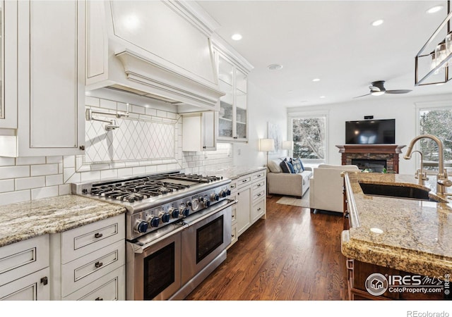 kitchen with double oven range, a sink, a ceiling fan, open floor plan, and white cabinetry