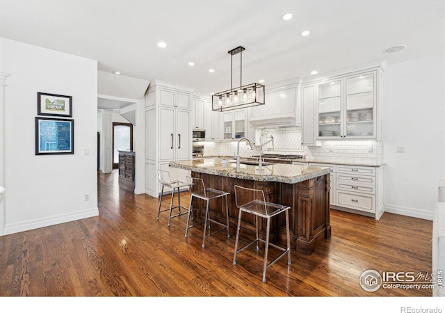 kitchen with an island with sink, a breakfast bar, backsplash, white cabinetry, and recessed lighting