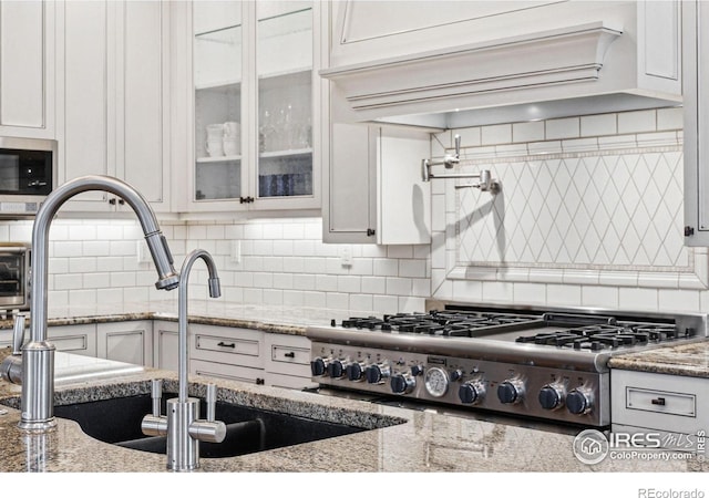 kitchen with backsplash, stainless steel appliances, glass insert cabinets, and white cabinetry