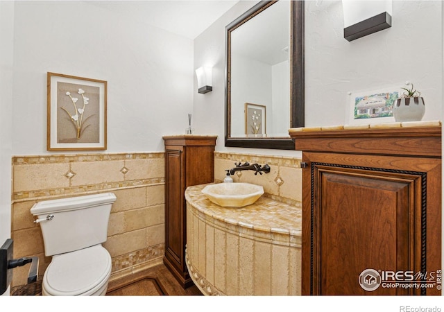 bathroom featuring tile walls, wainscoting, toilet, and vanity