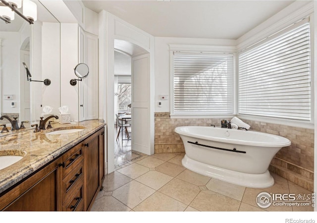 bathroom featuring tile walls, a freestanding bath, wainscoting, double vanity, and tile patterned flooring