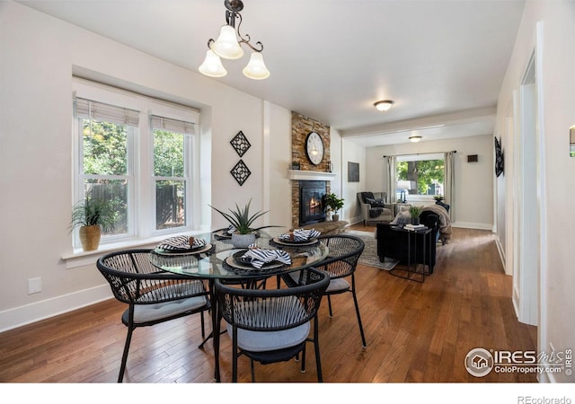 dining room featuring a stone fireplace, dark hardwood / wood-style floors, and an inviting chandelier