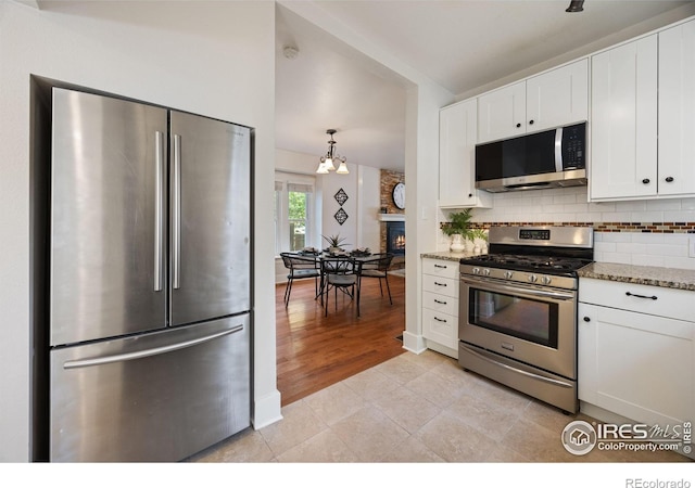 kitchen with appliances with stainless steel finishes, white cabinetry, backsplash, light stone countertops, and light tile patterned flooring