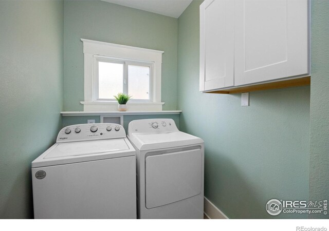 clothes washing area with separate washer and dryer and cabinets