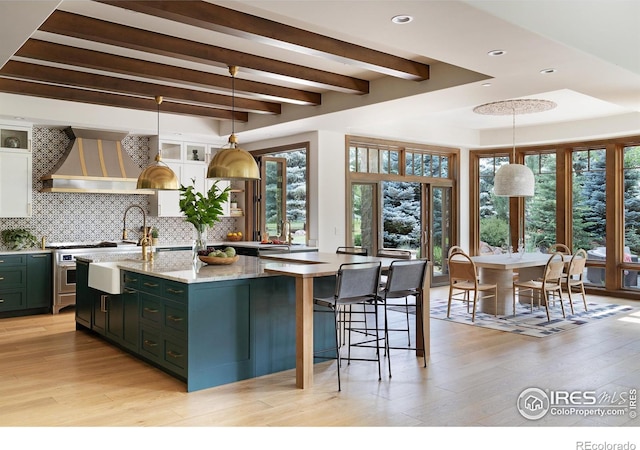 kitchen featuring light stone counters, premium range hood, an island with sink, and hanging light fixtures