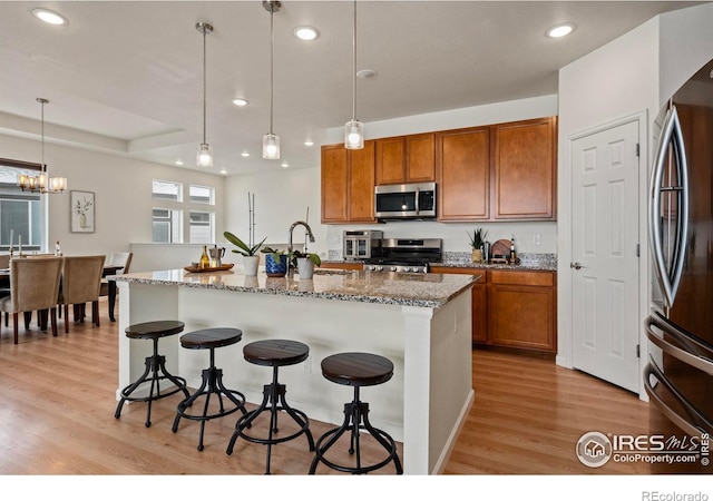 kitchen featuring decorative light fixtures, a kitchen breakfast bar, an island with sink, stainless steel appliances, and light stone countertops