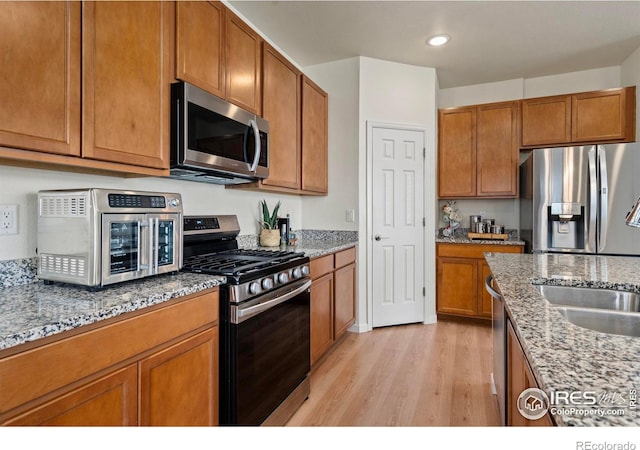 kitchen featuring stainless steel appliances, light stone countertops, sink, and light hardwood / wood-style floors