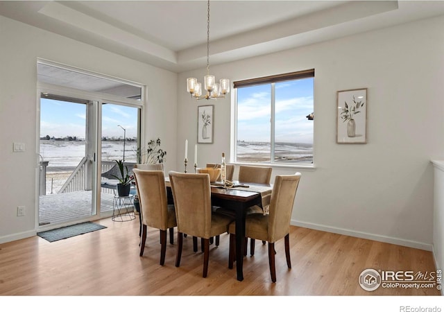 dining area with a tray ceiling, light wood-type flooring, a chandelier, and a water view