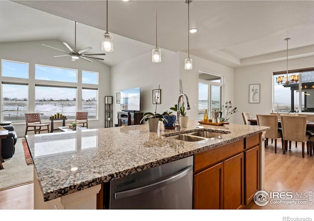 kitchen with dishwasher, sink, light stone counters, light hardwood / wood-style floors, and a center island with sink