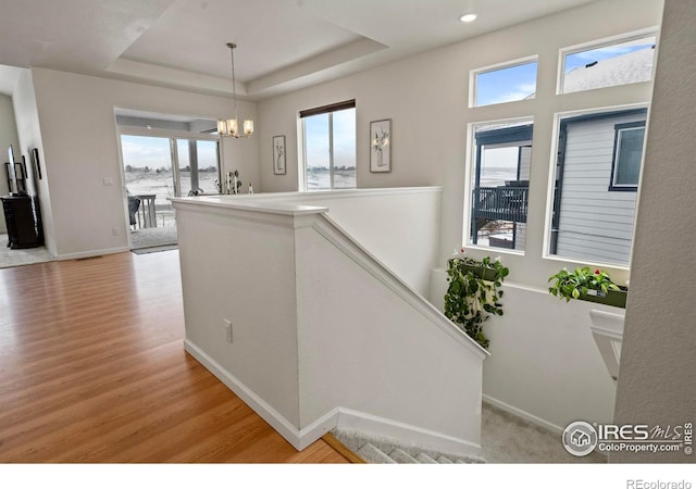 hall featuring a tray ceiling, light hardwood / wood-style flooring, and a notable chandelier