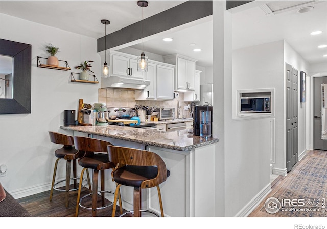 kitchen featuring a breakfast bar area, appliances with stainless steel finishes, white cabinetry, light stone countertops, and kitchen peninsula