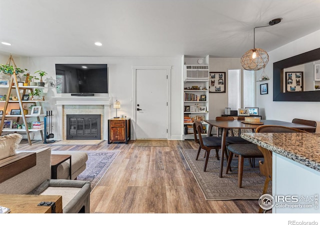 living room featuring wood-type flooring, a tiled fireplace, and an AC wall unit