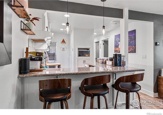 kitchen with a breakfast bar area, decorative light fixtures, light wood-type flooring, light stone countertops, and white cabinets