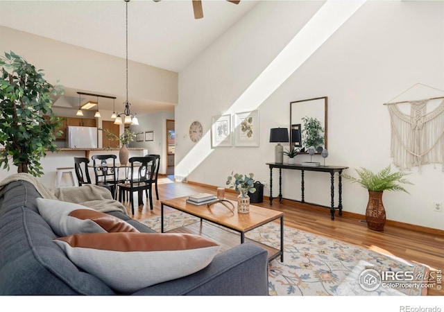 living room with a towering ceiling, ceiling fan, and light hardwood / wood-style flooring