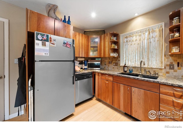 kitchen featuring sink, light wood-type flooring, stainless steel appliances, light stone countertops, and decorative backsplash