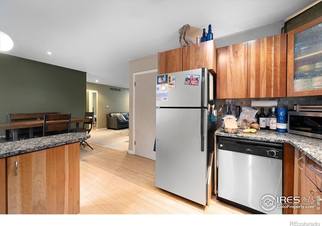 kitchen featuring tasteful backsplash, appliances with stainless steel finishes, light hardwood / wood-style flooring, and dark stone counters