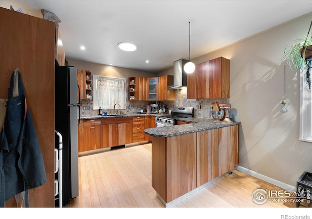 kitchen with pendant lighting, tasteful backsplash, kitchen peninsula, stainless steel appliances, and wall chimney range hood