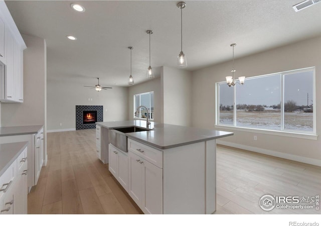 kitchen with sink, light hardwood / wood-style flooring, white cabinetry, a kitchen island with sink, and a tiled fireplace