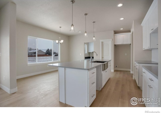 kitchen with sink, decorative light fixtures, light wood-type flooring, an island with sink, and white cabinets