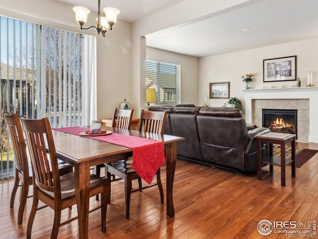 dining area with a tiled fireplace, a notable chandelier, and wood-type flooring