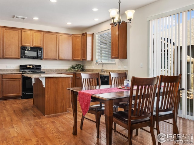 kitchen with decorative light fixtures, wood-type flooring, black appliances, and a kitchen island