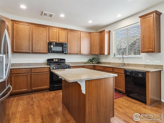 kitchen with sink, a kitchen island, light stone countertops, light hardwood / wood-style floors, and black appliances