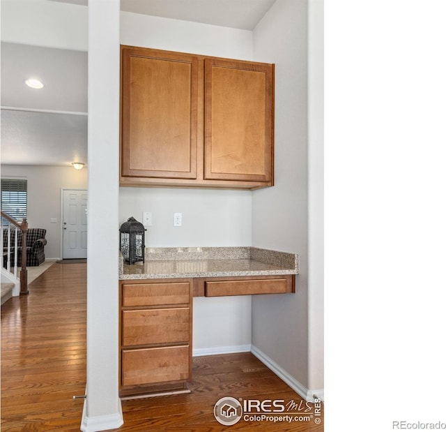 kitchen featuring light stone countertops, built in desk, and dark hardwood / wood-style flooring