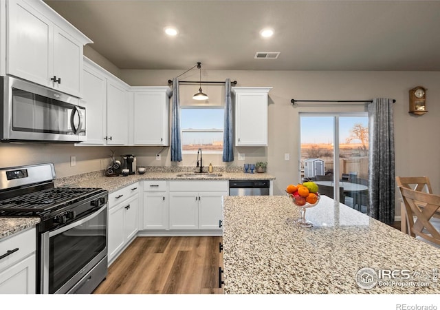 kitchen with sink, appliances with stainless steel finishes, hanging light fixtures, light stone countertops, and white cabinets