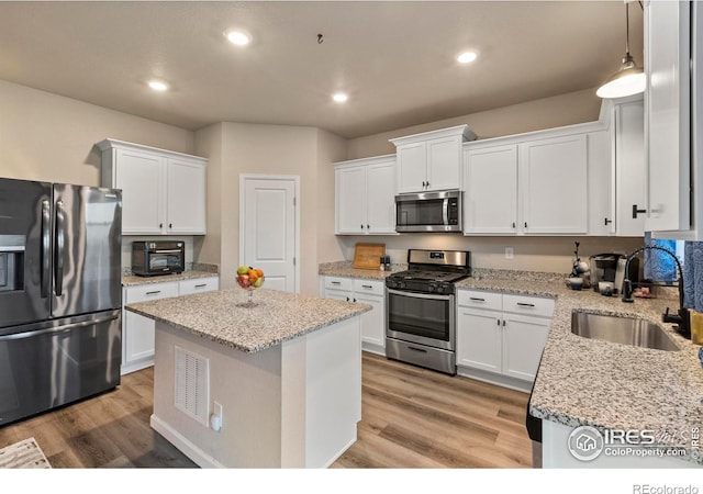 kitchen with appliances with stainless steel finishes, white cabinetry, sink, a center island, and light stone countertops