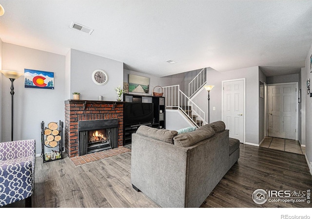 living area with stairs, a brick fireplace, wood finished floors, and visible vents