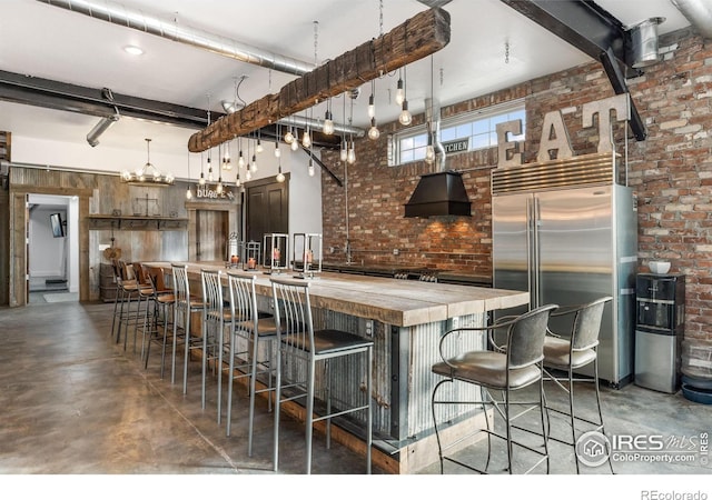 kitchen featuring brick wall, a breakfast bar area, built in refrigerator, custom exhaust hood, and a kitchen island with sink