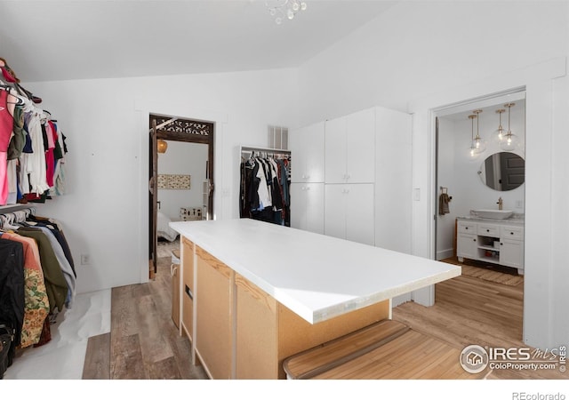 walk in closet with vaulted ceiling, sink, and light hardwood / wood-style flooring