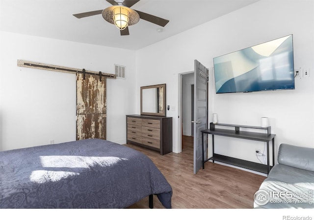 bedroom with hardwood / wood-style flooring, ceiling fan, and a barn door