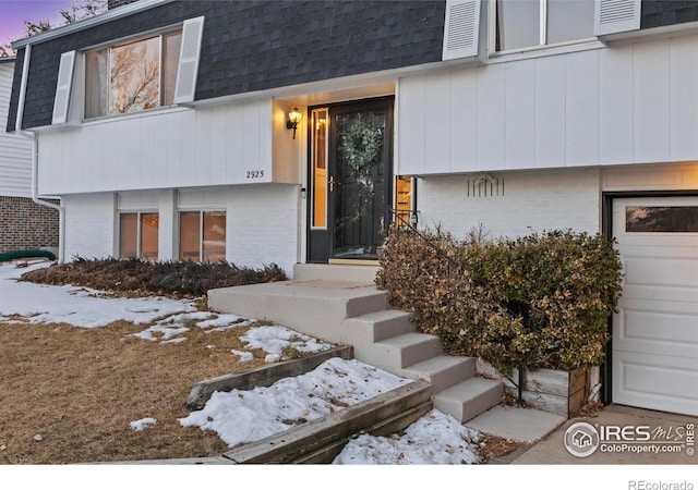 snow covered property entrance featuring a garage