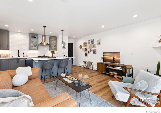 living room featuring sink, baseboard heating, and light hardwood / wood-style flooring