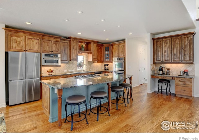 kitchen featuring appliances with stainless steel finishes, backsplash, a kitchen bar, dark stone counters, and light wood-type flooring