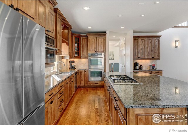 kitchen featuring appliances with stainless steel finishes, sink, dark stone countertops, decorative backsplash, and light hardwood / wood-style flooring