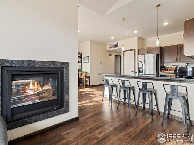 kitchen featuring a multi sided fireplace, dark hardwood / wood-style floors, pendant lighting, a breakfast bar area, and stainless steel refrigerator with ice dispenser