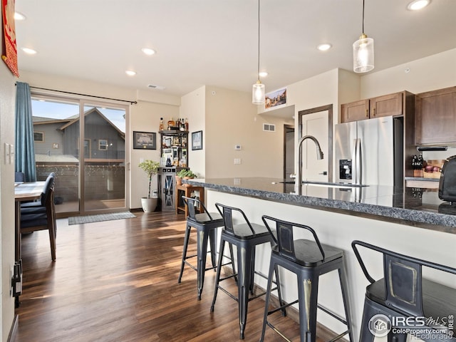 kitchen featuring a breakfast bar, pendant lighting, dark hardwood / wood-style flooring, dark stone counters, and stainless steel refrigerator with ice dispenser