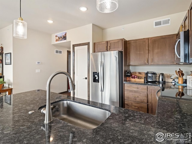 kitchen with appliances with stainless steel finishes, decorative light fixtures, sink, and dark stone countertops