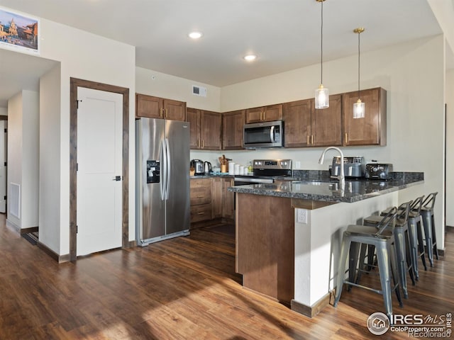 kitchen with pendant lighting, sink, dark stone countertops, kitchen peninsula, and stainless steel appliances