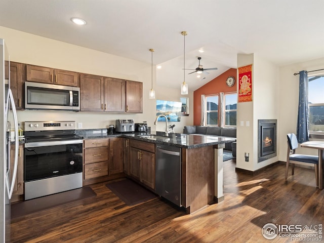 kitchen with sink, dark stone countertops, stainless steel appliances, decorative light fixtures, and kitchen peninsula