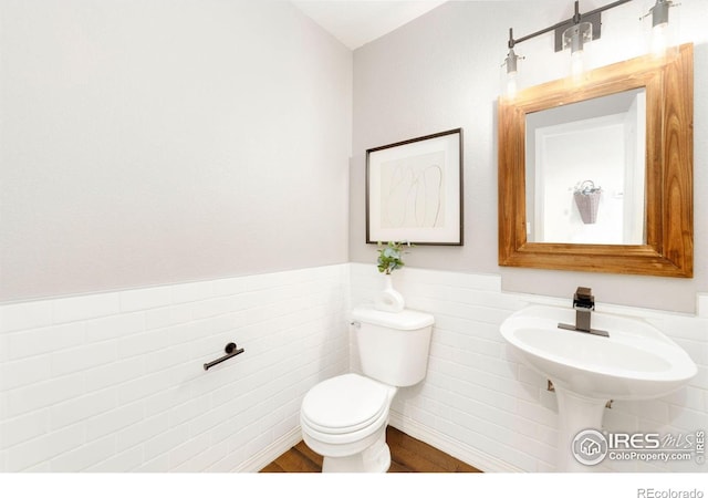 half bathroom featuring wainscoting, wood finished floors, toilet, and tile walls