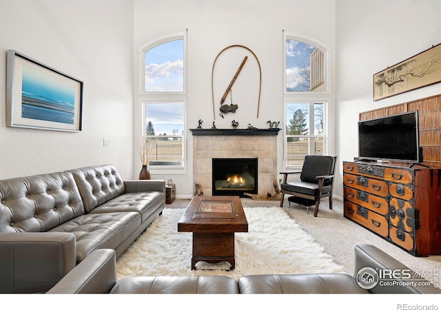 carpeted living room featuring a tiled fireplace and a high ceiling