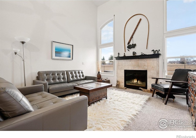 living room featuring a tiled fireplace, carpet, and a high ceiling