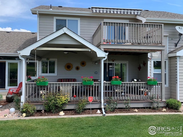 back of property featuring ceiling fan, a lawn, and a balcony