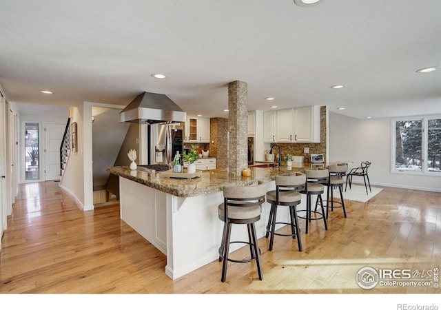 kitchen featuring decorative backsplash, light wood-style floors, a breakfast bar area, and island range hood