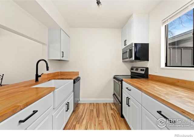 kitchen with appliances with stainless steel finishes, butcher block counters, sink, and white cabinets